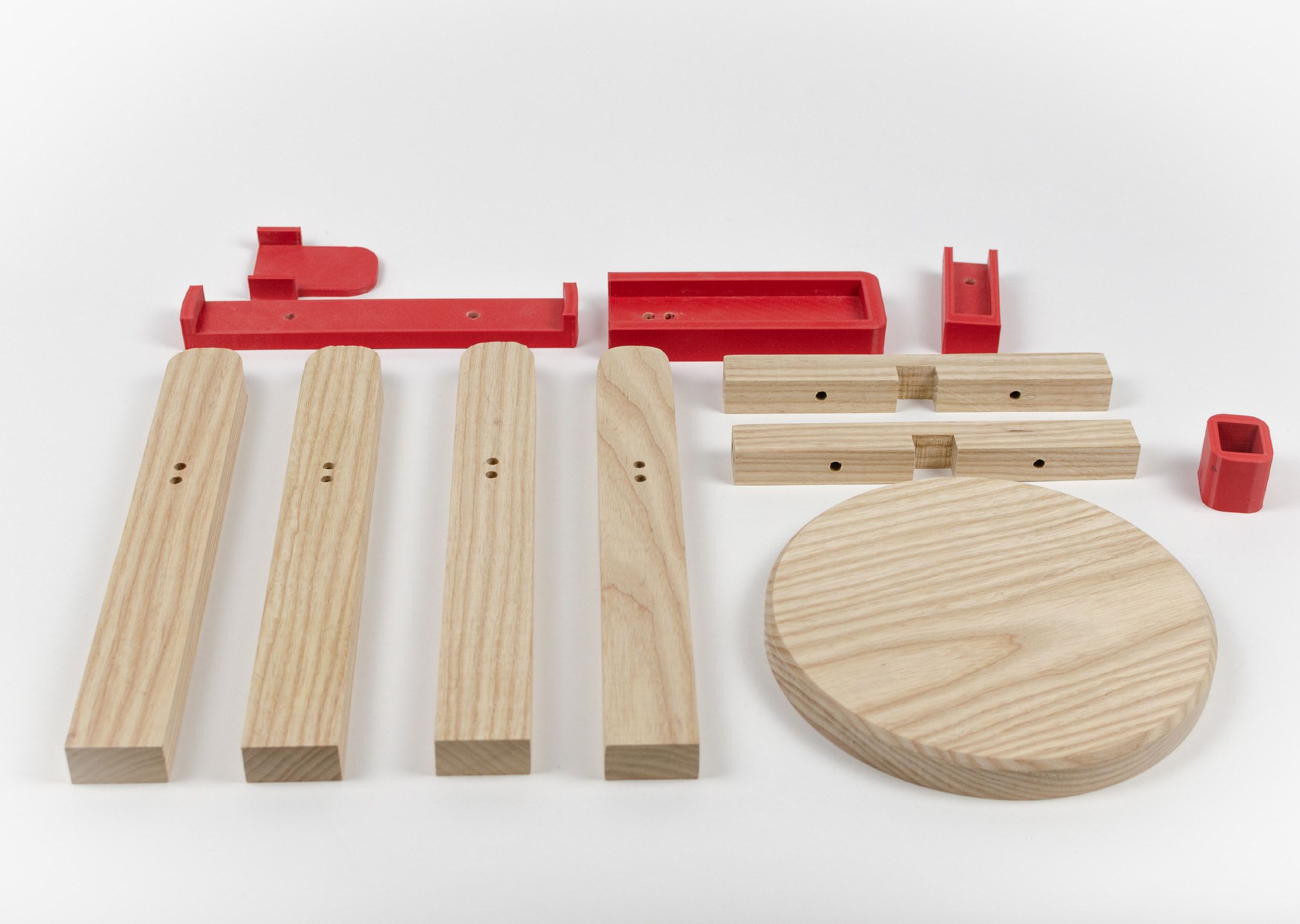 The plant stand’s parts laid out on white: four wooden legs, two cross beams, a round top and five red 3D-printed jigs.