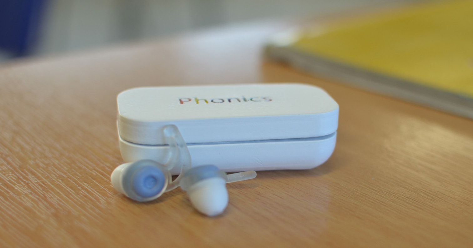 The 3D-printed prototype: a white case printed with “Phonics” and two earbuds with light blue tips on a wooden desk.