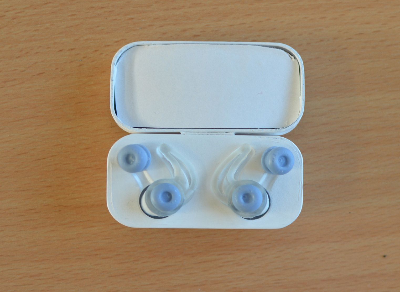 The open prototype case from above, holding two earbuds with clear hooks and two spare light blue ear tips.